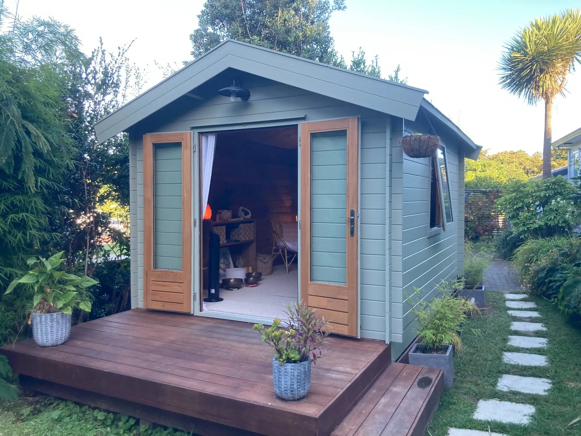 Garden cabin painted sage green with oiled cedar doors